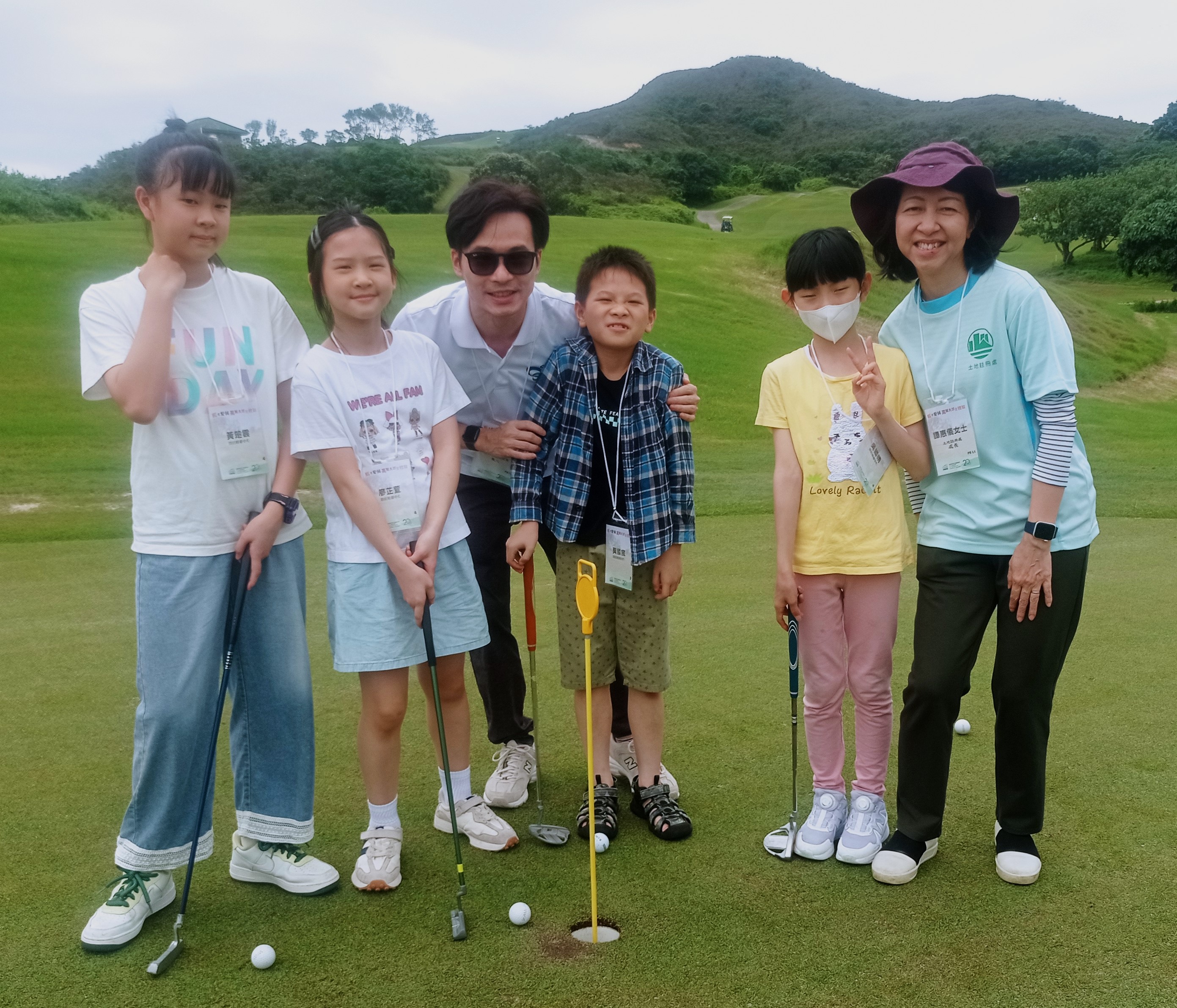 土 地 注 册 处 处 长 谭 惠 仪 女 士 （ 右 一 ） 陪 伴 儿 童 在 赛 马 会 滘 西 洲 公 众 高 尔 夫 球 场 体 验 打 高 尔 夫 球 的 乐 趣